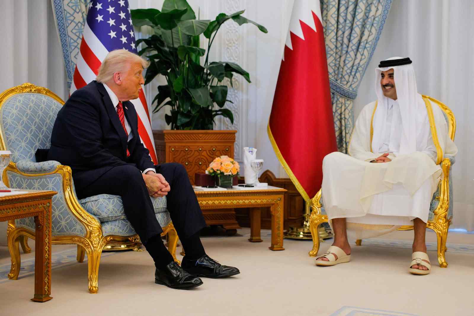 Two men seated in chairs with various flags displayed behind them.